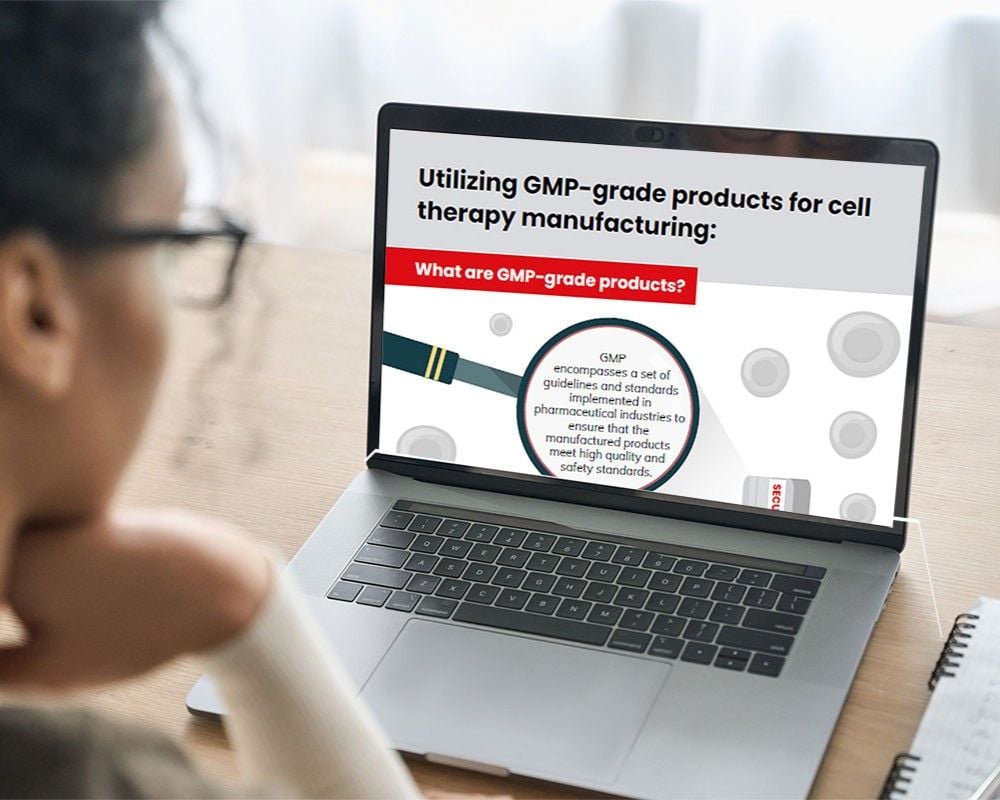 A woman looking at a laptop displaying an infographic titled 'Utilizing GMP-grade products for cell therapy manufacturing